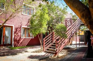 温特和克Windhoek Gardens Boutique Hotel的通往粉红色的树木建筑的木楼梯