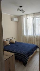 布尔加斯Сарафово Център的一间卧室配有一张带蓝色床单的床和一扇窗户。