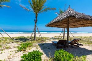 岘港Ocean Beach Villas Danang的一个带草伞和椅子的海滩和棕榈树