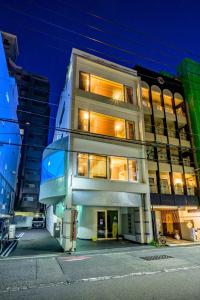广岛Hiroshima Wabisabi hostel 広島ワビサビ ホステル的一座高大的白色建筑,晚上有窗户点亮