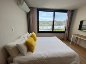 济州市Living in Jeju Island的卧室配有白色床、黄色枕头和窗户