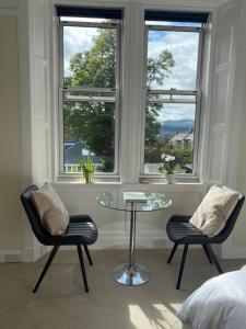 爱丁堡Tranquil Haven Murrayfield的一间设有两把椅子、一张玻璃桌和两扇窗户的房间