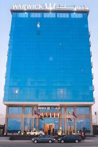 吉达Warwick Hotel Jeddah的一座蓝色的建筑,前面有汽车停放