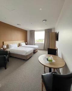奥克兰Manha Hotel Auckland Airport的酒店客房带两张床和一张桌子以及椅子。
