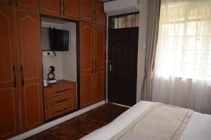 内罗毕Cozy Stead的一间卧室配有一张床、一台电视和木制橱柜。