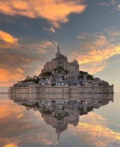 Saint-Vigor-le-GrandLe Chalet de St Vigor的日落时分在水中的一个岛上的城堡