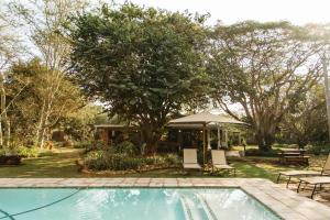 MkuzeBiweda Nguni Lodge的庭院内的游泳池,配有桌椅