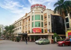 河内Kim Liên - Số 7 Đào Duy Anh - by Bay Luxury Hotel的一座大型建筑,前面有汽车停放