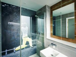 利兹利兹市中心竞技场宜必思尚品酒店的一间玻璃淋浴间的浴室,浴室里有人站在床上