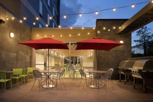 罗斯维尔Home2 Suites by Hilton Roseville Minneapolis的庭院里配有两张桌子和椅子以及红伞