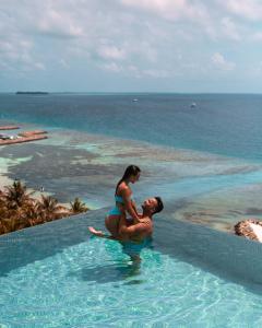 马富施Kaani Palm Beach的坐在海洋附近的游泳池里的男人和女人