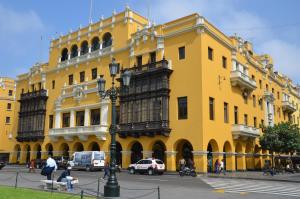 利马Most Central Place in Lima的一座黄色的建筑,前面有汽车停放