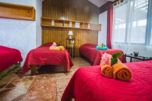 安加罗阿Cabañas & Hostal Tojika的一间设有三张床的房间,配有红色床单和动物填充物