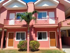 麦克坦Vacation Town House Near Mactan Cebu Airport的一座粉红色的房子,前面有一棵棕榈树