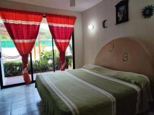 锡瓦塔塔内霍J.B.酒店的一间卧室配有一张带红色窗帘的床和一扇窗户
