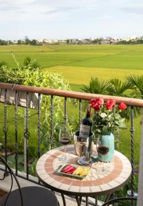 会安Maison Fleur Luxury Hoi An的阳台上的桌子上放着两杯葡萄酒和鲜花