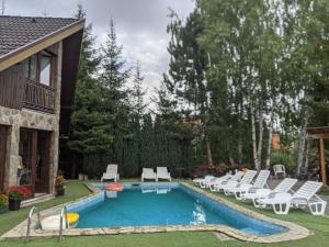 兹拉蒂博尔Vila Zlatibor的一个带白色椅子的游泳池以及一座房子