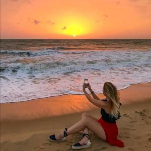 乌斯维塔克伊亚瓦Bivon Reach By Travel Corners的坐在海滩上拍摄日落景象的女人