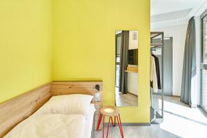 科隆MEININGER Hotel Köln West的卧室拥有黄色的墙壁,配有一张床和凳子