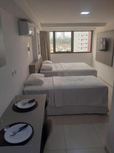若昂佩索阿Manaíra Apart Hotel的酒店客房设有两张床和一张带盘子的桌子。