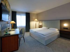 格拉Mercure Hotel Gera City的酒店客房设有一张大床和一张书桌。