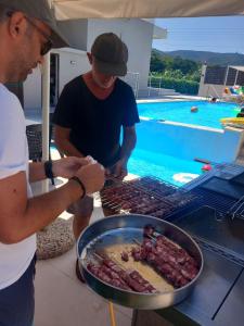 SkinésGiannis Villa的两个男人在游泳池旁的烧烤架上准备食物