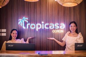 科隆Tropicasa Coron Resort & Hotel的两个女人站在一个柜台前,站在一个标志前