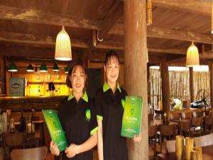 Hương Bá ThướcPu Luong Homestay & Tours的两名妇女站在餐厅里,持绿色标志