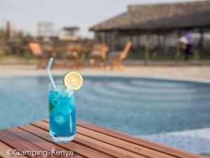 Naro MoruGlamping Kenya Mt. Kenya Lodge的坐在游泳池旁的桌子上,喝着一杯蓝色的饮料,并把柠檬片放在桌上