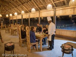 Naro MoruGlamping Kenya Mt. Kenya Lodge的厨师站在餐厅里,有人坐在桌子旁