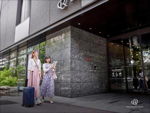 京都京都四条乌丸大和ROYNET酒店的两名妇女站在一幢建筑物前,手提箱