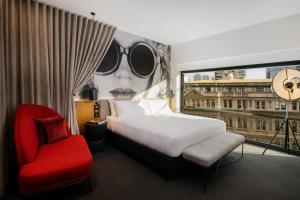 墨尔本Hotel Indigo Melbourne on Flinders, an IHG Hotel的一间卧室配有一张床、一张红色椅子和一个窗户