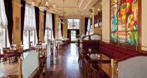莱比锡莱比锡城维克特雷斯登斯酒店的餐厅设有桌椅,墙上挂有绘画作品