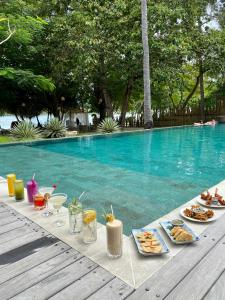 吉利阿萨汉Amahelia Luxury Resort & Restaurant - Gili Asahan的游泳池旁的餐桌,供应食物和饮料