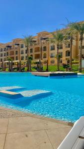 开罗Ultra Luxury 3BR with Pools ,Sports ,Dining in Gated compound, Close to all sites的一座种植了棕榈树的大型蓝色游泳池和一座建筑