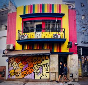 科尔多瓦Lacandona Hostel的两个人走过一座色彩缤纷的建筑,涂鸦