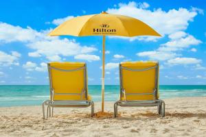 迈阿密海滩Hilton Cabana Miami Beach Resort的海滩上遮阳伞下的两张黄色沙滩椅