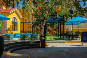 会安La Charm Hoi An Hotel & Spa的黄色建筑前的树,上面有蓝色的伞