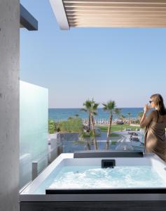 罗希姆诺Nautilux Rethymno by Mage Hotels的站在浴缸中一边欣赏海景的女人
