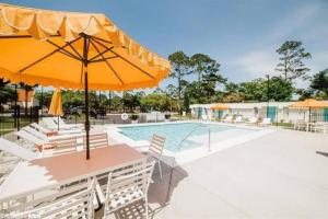 格尔夫海岸Gulf Shores Getaway steps away from the pool!的一个带桌子、遮阳伞和椅子的游泳池
