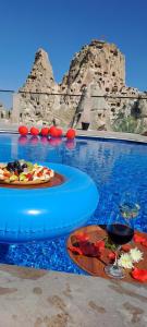 乌奇希萨尔赫尔墨斯窑洞酒店的一座游泳池,里面装有一盘食物和一杯葡萄酒