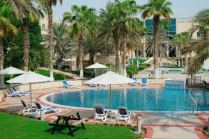 阿布扎比Metropolitan Al Mafraq Hotel的一个带椅子和遮阳伞的游泳池以及棕榈树
