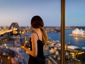 悉尼The Sebel Quay West Suites Sydney的站在窗户前的女人,拿着酒杯