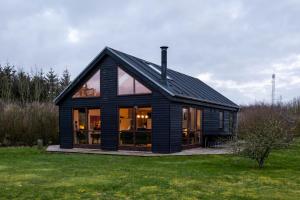 斯凯恩Vidunderlig fritidshus ved Skov og Golfbane的一座黑色房子,在田野上设有大窗户