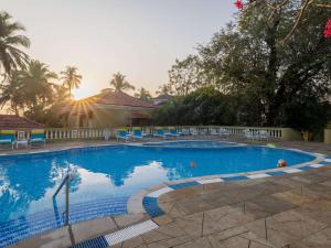 果阿旧城Mercure Goa Devaaya Resort的一座蓝色的大型游泳池,里面设有蓝色的椅子和树木
