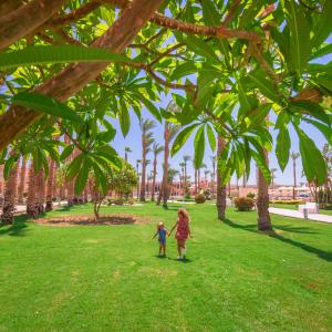 赫尔格达Beach Albatros Aqua Park - Hurghada的两个孩子在棕榈树下的公园里散步