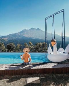 库布盼洛坎Sari Sky Bali的坐在有天鹅的游泳池里,戴着草帽的人
