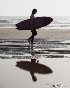 阿加迪尔Desart Hostel的一个人在海滩上用冲浪板行走