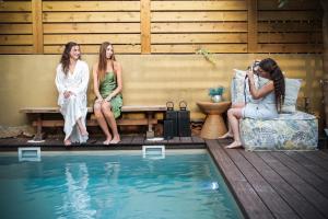 Kfar YonaLaethos - the house of fun.的三个女人坐在游泳池旁的长椅上
