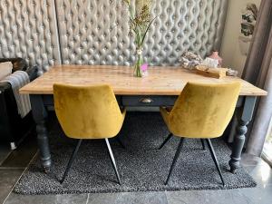莱森Bed & Breakfast "aan de banis"的墙上有一张木桌和两把黄色椅子